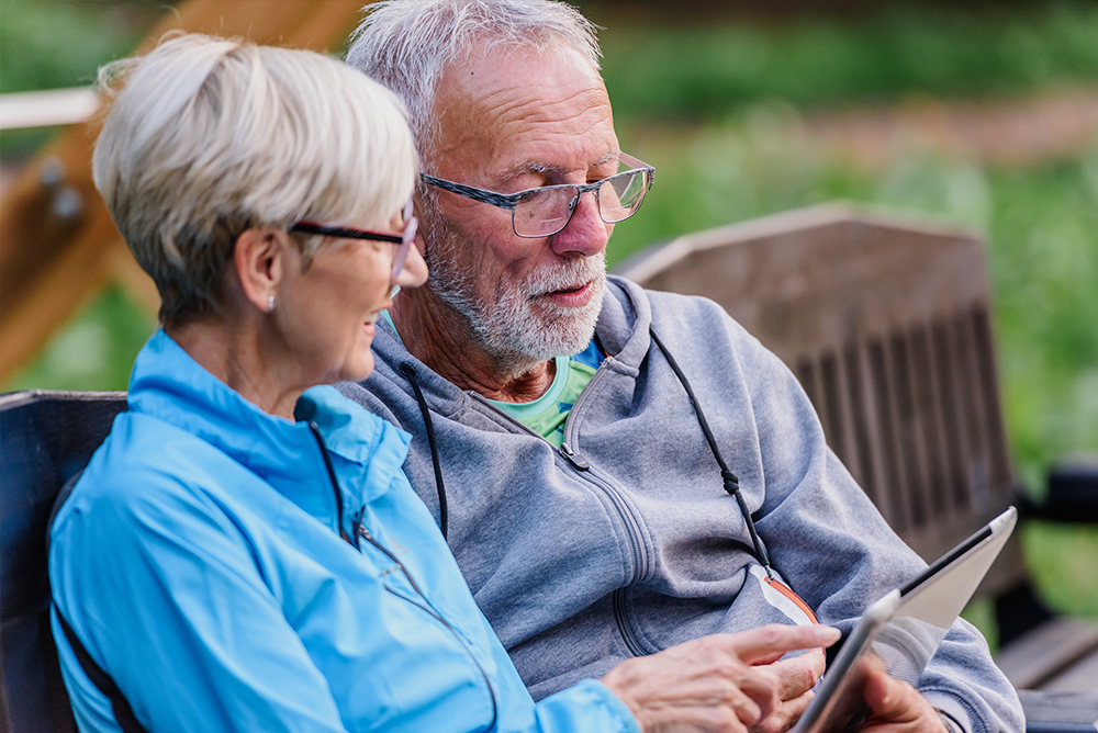 Middle aged couple sitting on a bench looking at a tablet