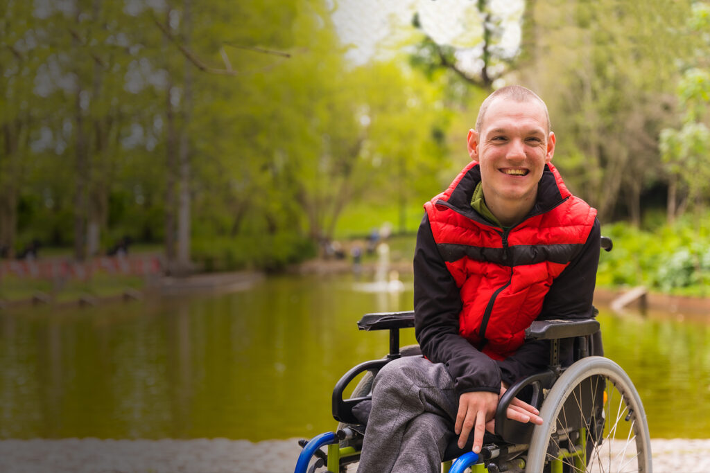ALS patient in red vest outdoors near a pond